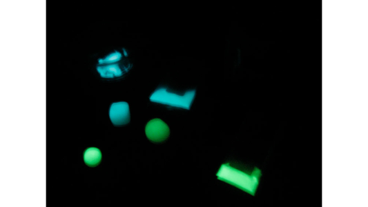 Pieces of InstaMorph moldable plastic shown glowing in the dark, some green, some blue.