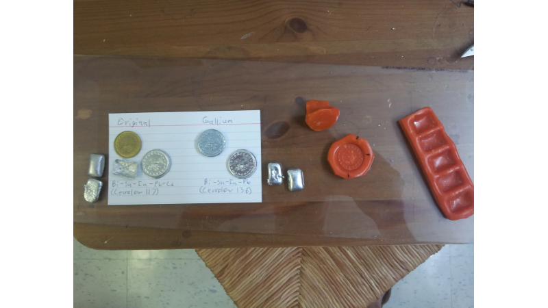 White index card showing original coins and coins made with silver-colored InstaMorph moldable plastic. Also shown are the red molds used to create the coins.